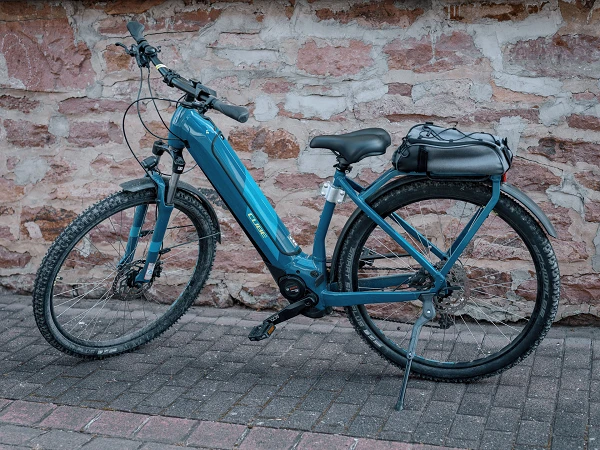 Ein grünes E-Bike steht auf einem gepflasterten Weg vor einer rustikalen Steinmauer. Es hat einen robusten Rahmen, einen stabilen Gepäckträger und einen akzentuierten Motor.